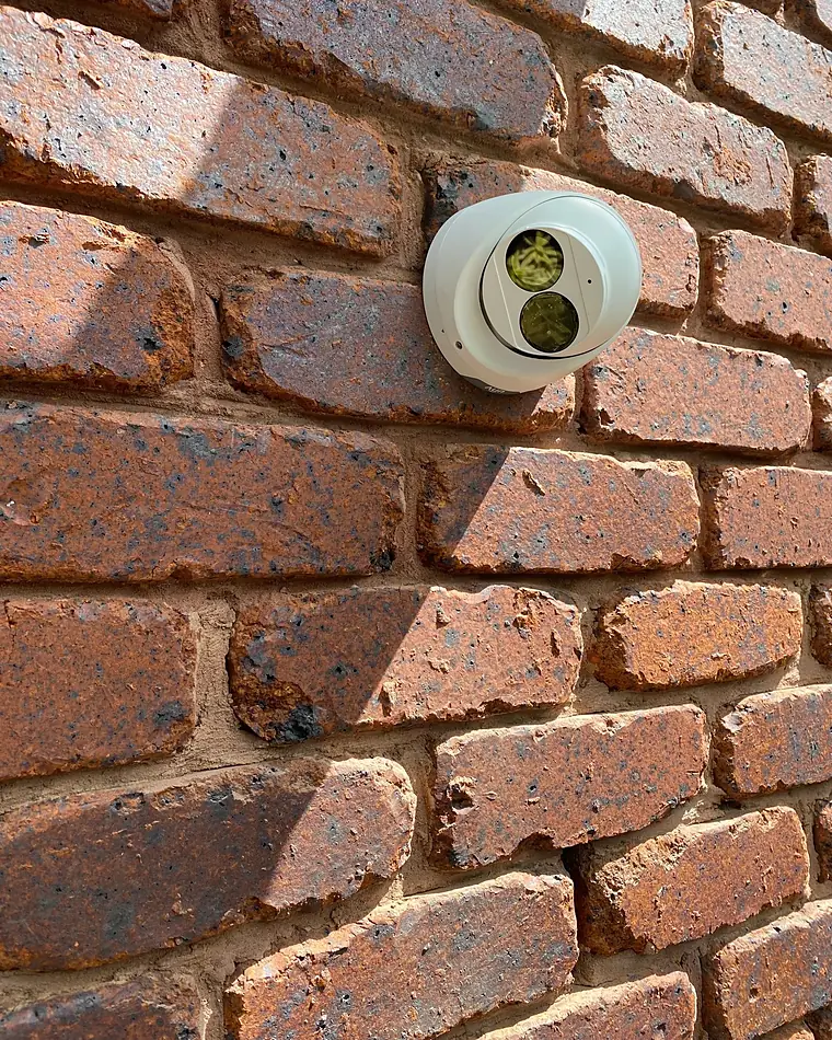 A white turret security camera fixed to a red face-brick wall