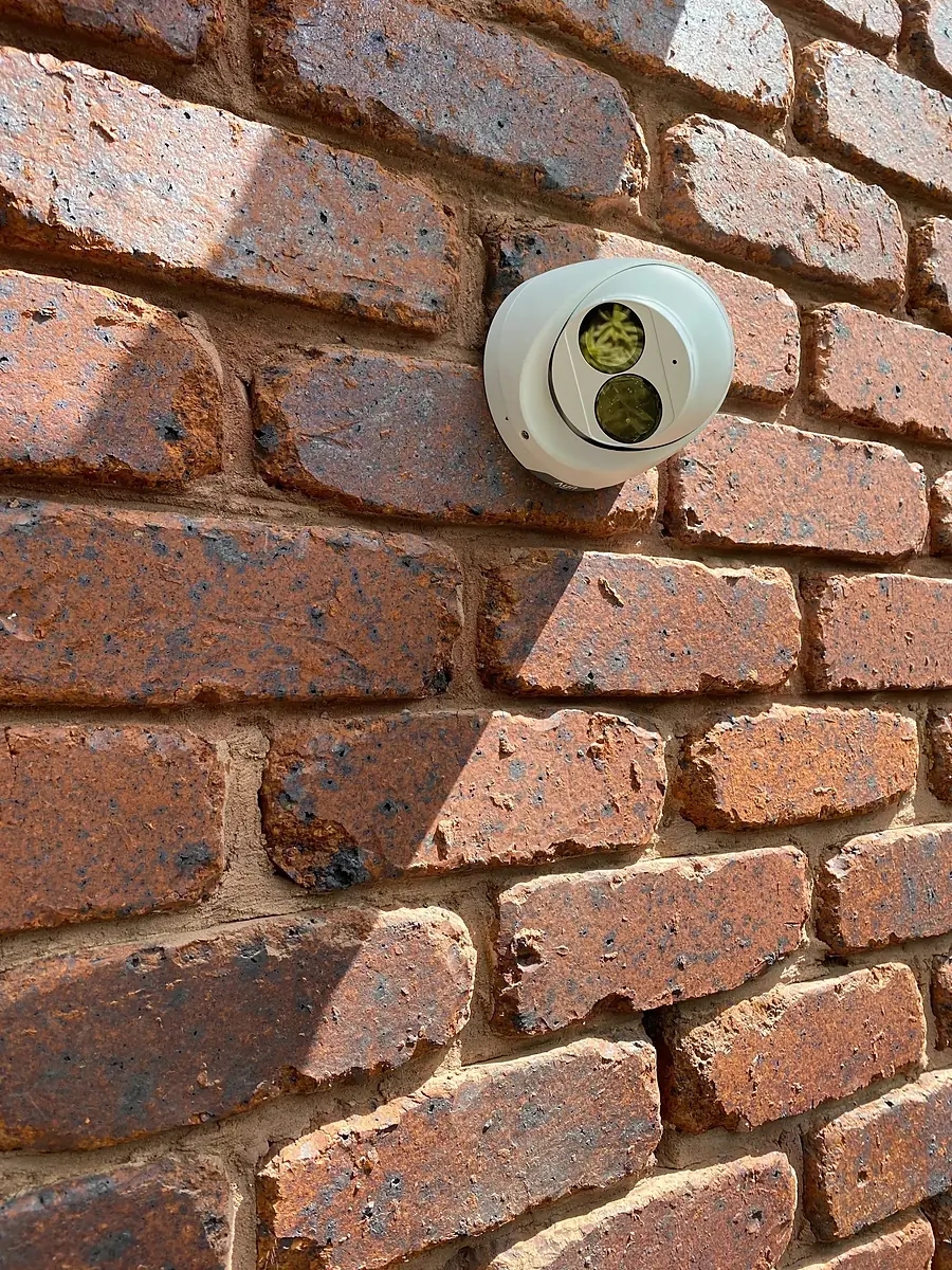 A white turret security camera fixed to a red face-brick wall