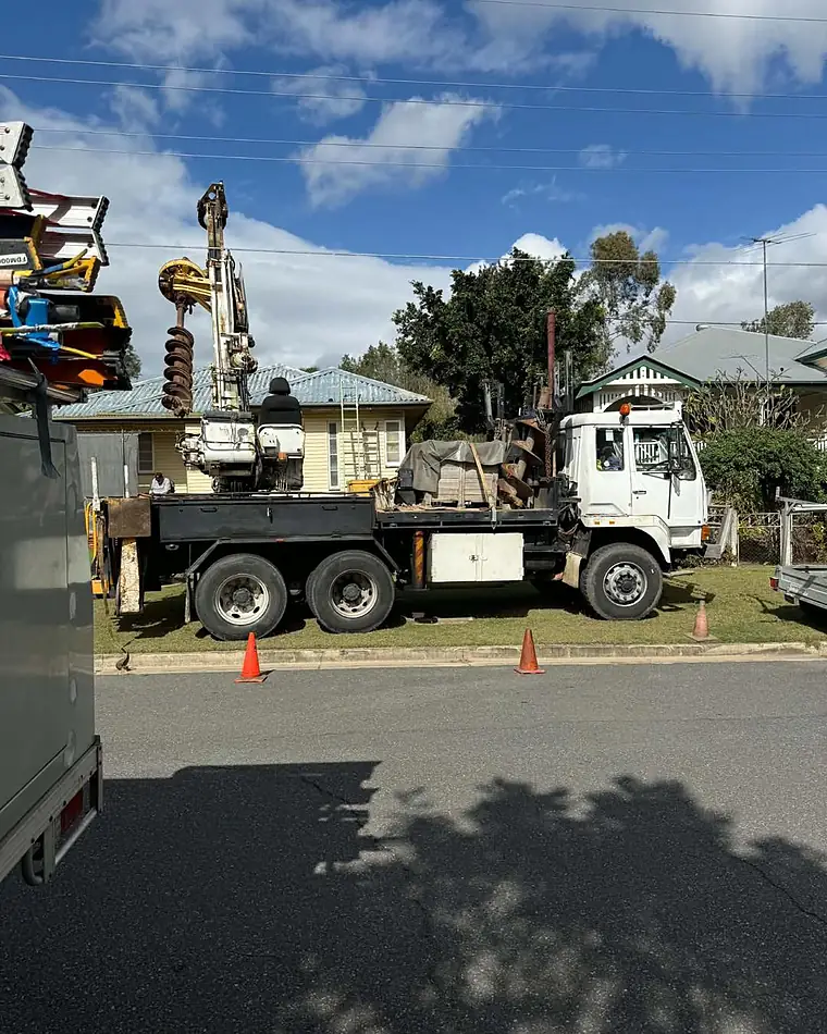 A pole-drilling truck and work ute parked at a street job