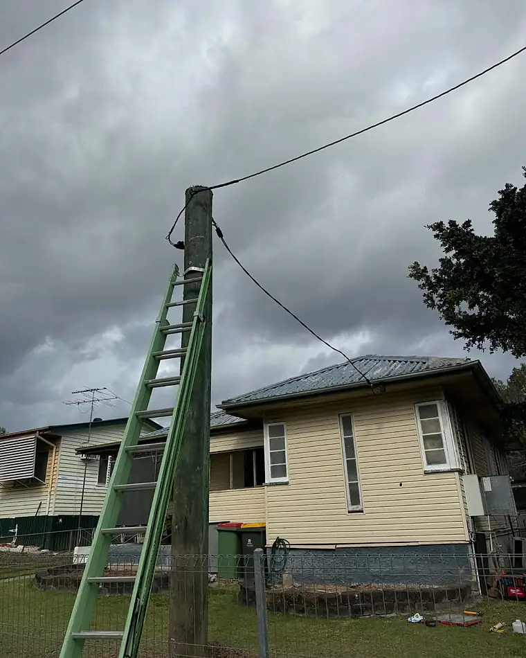 A new property pole with a ladder against it beside a yellow weatherboard house