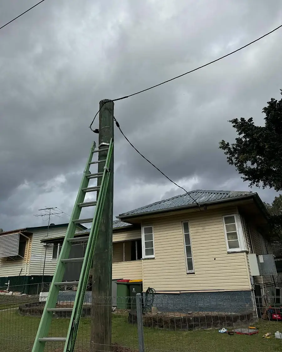 A new property pole with a ladder against it beside a yellow weatherboard house