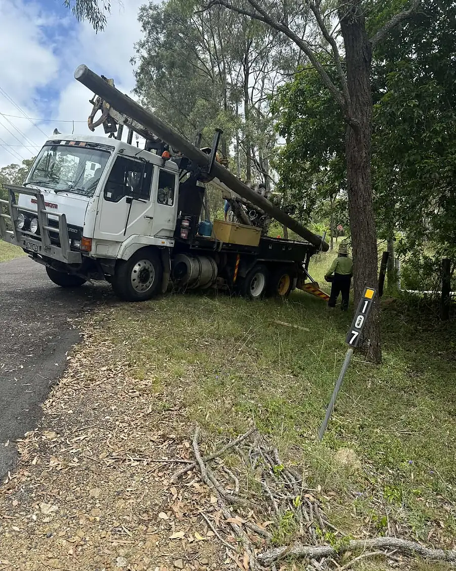 A pole truck lifting a new power pole beside a bush road