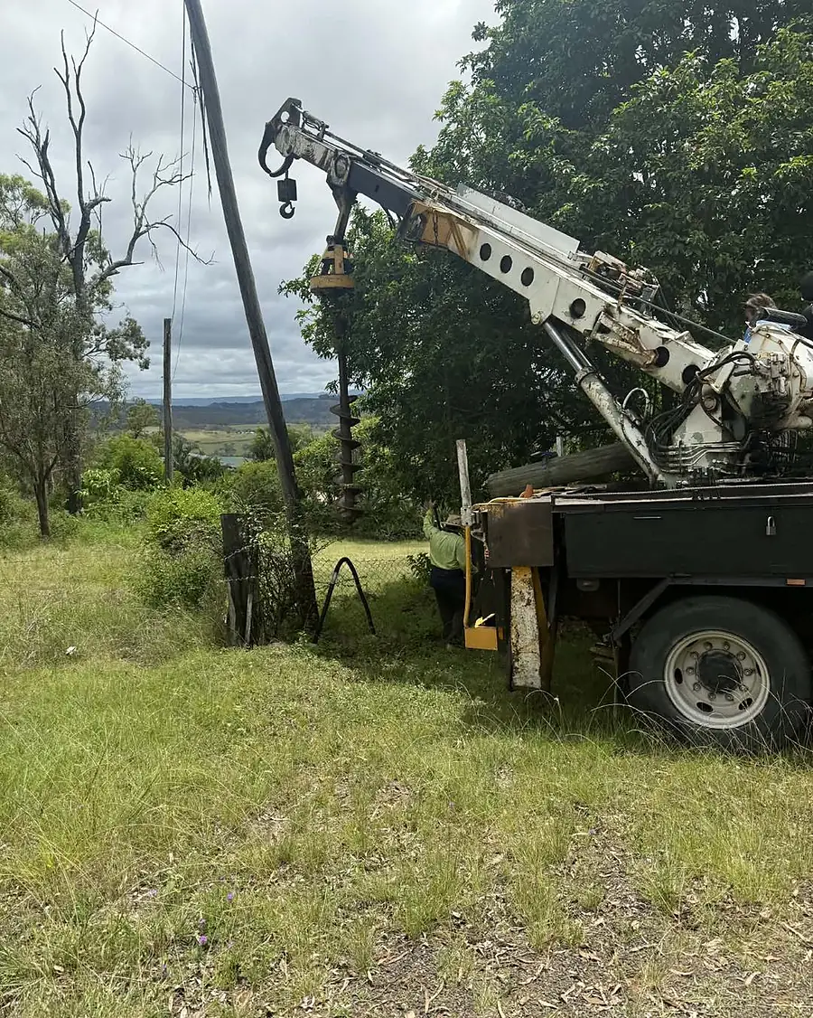 A crane truck drilling the hole for a new pole on a hillside