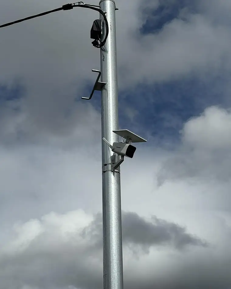 A solar-powered camera on a galvanised pole against a cloudy sky