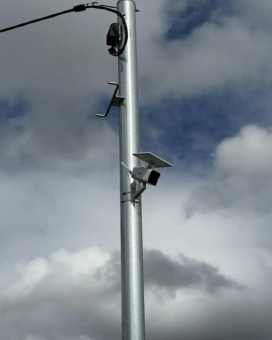 A solar-powered camera on a galvanised pole against a cloudy sky