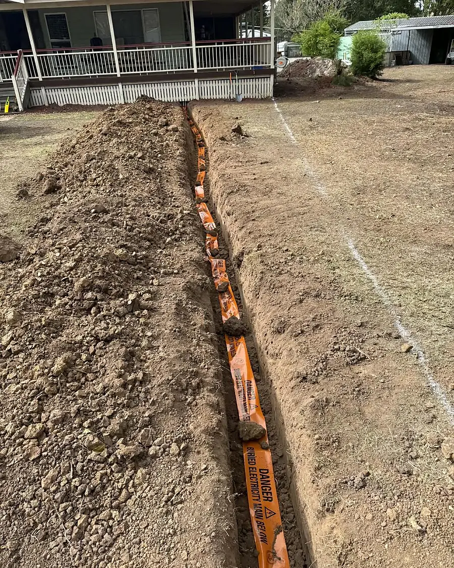 A cable trench with orange danger tape running towards a house