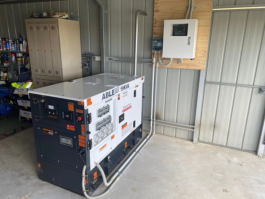 A diesel standby generator in a shed with its changeover board on the wall